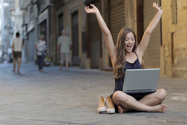 Woman Raising Her Hands Up While Sitting on Floor With Macbook Pro