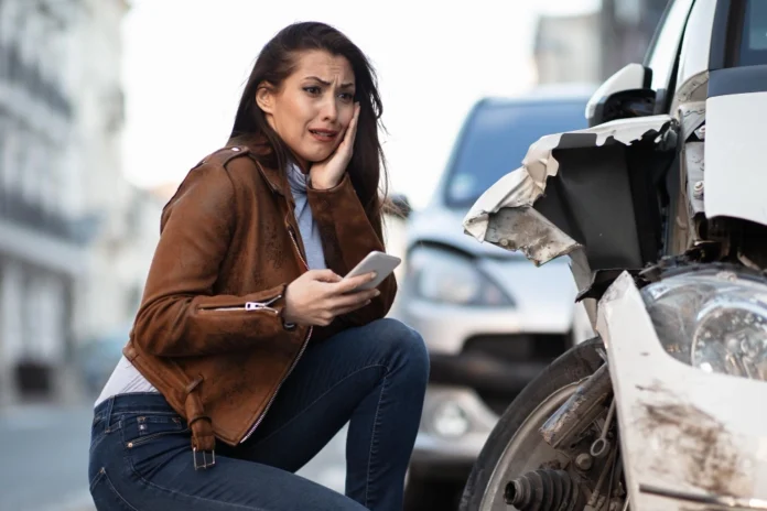 Young woman feeling shocked by car damage after an accident