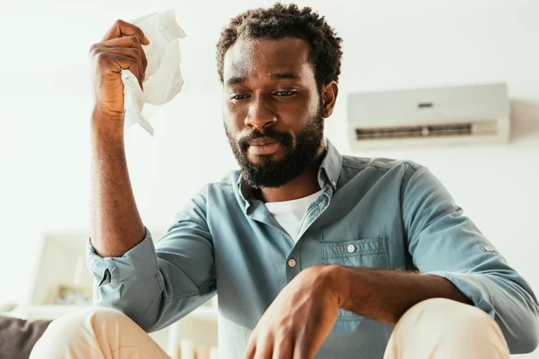 A man is sitting in front of the AC with a paper in his hand